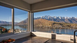 A kitchen with large windows offering a view of a lake and mountains. - Castle Cliff Lodge | Spa Pool + Sauna | Games Room (Queenstown)