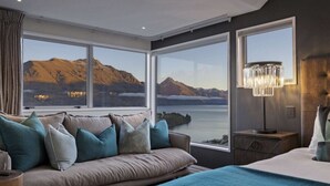 A bedroom with a large window, a bed, a nightstand, and a lamp. - Castle Cliff Lodge | Spa Pool + Sauna | Games Room (Queenstown)