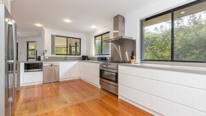 Una cocina moderna con armarios blancos, una campana extractora de acero inoxidable y un amplio ventanal con vistas a zonas verdes.