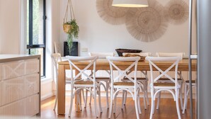 Un comedor con una mesa de madera, sillas blancas y una planta colgante.