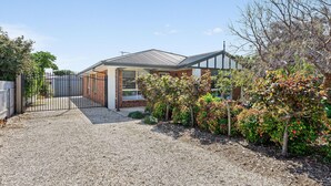 A modern house with a gravel driveway, a metal gate, and a variety of shrubs and trees. - Aldinga Rose - Aldinga Beach - C21 SouthCoast Holidays (Aldinga Beach)