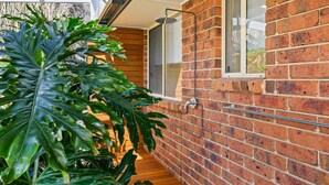 A modern house with a brick exterior, a wooden deck, and a large plant. - Aldinga Rose - Aldinga Beach - C21 SouthCoast Holidays (Aldinga Beach)