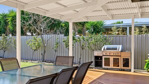An outdoor patio with a glass-top table and chairs, a barbecue grill, and a wooden deck. - Aldinga Rose - Aldinga Beach - C21 SouthCoast Holidays (Aldinga Beach)