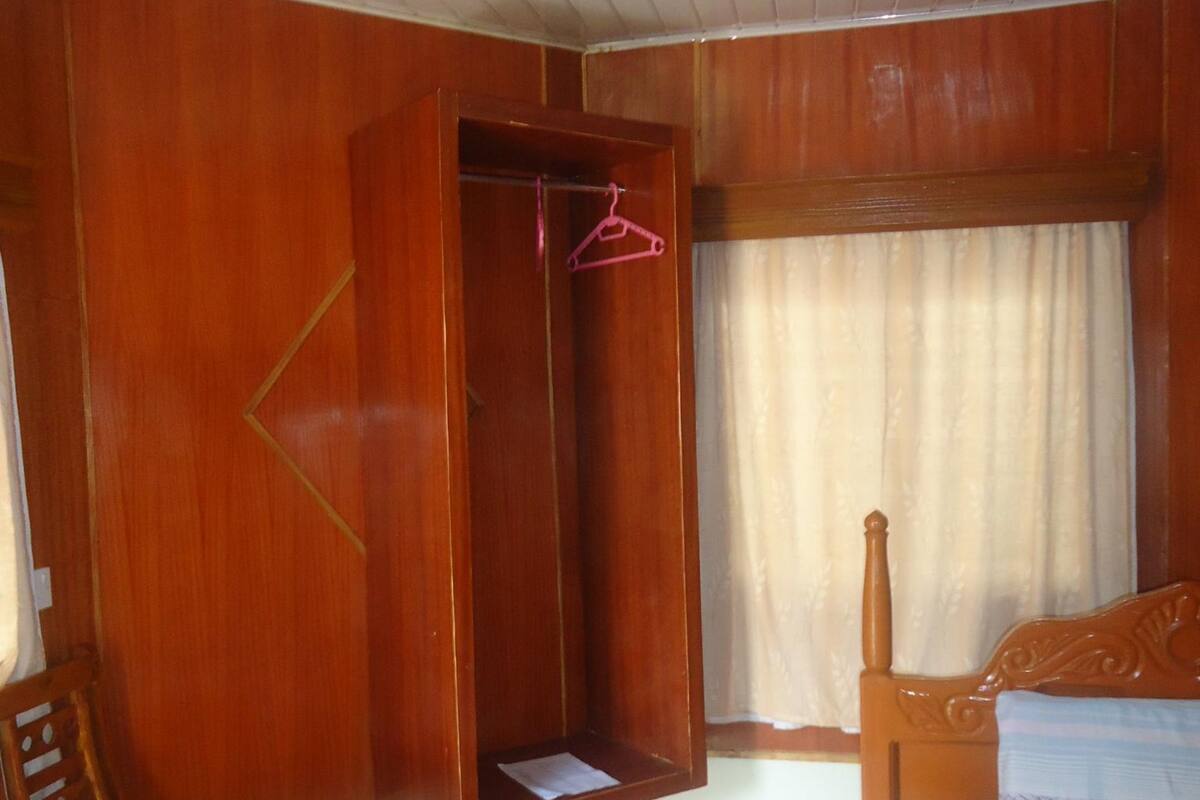 A room with a bed, a wooden wardrobe, a table, and a chair.