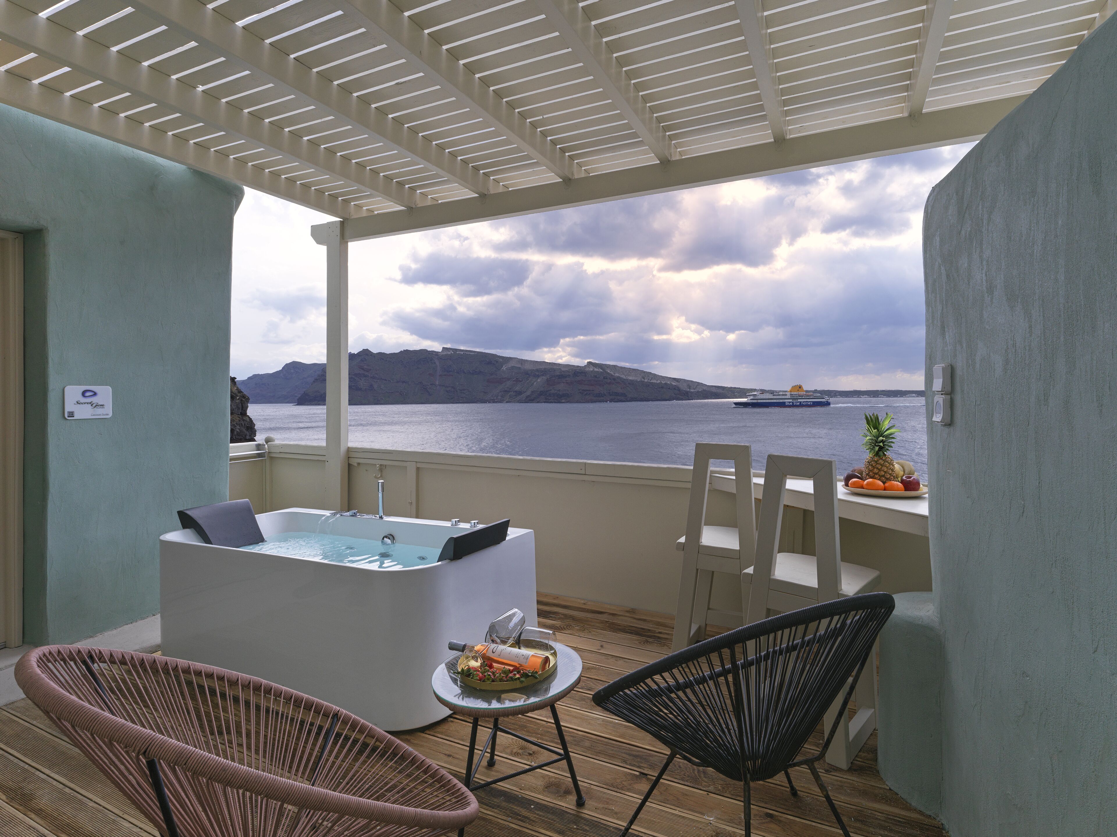 Een balkon met een hottub, rieten stoelen, een klein tafeltje met fruit, en uitzicht op zee en kliffen.