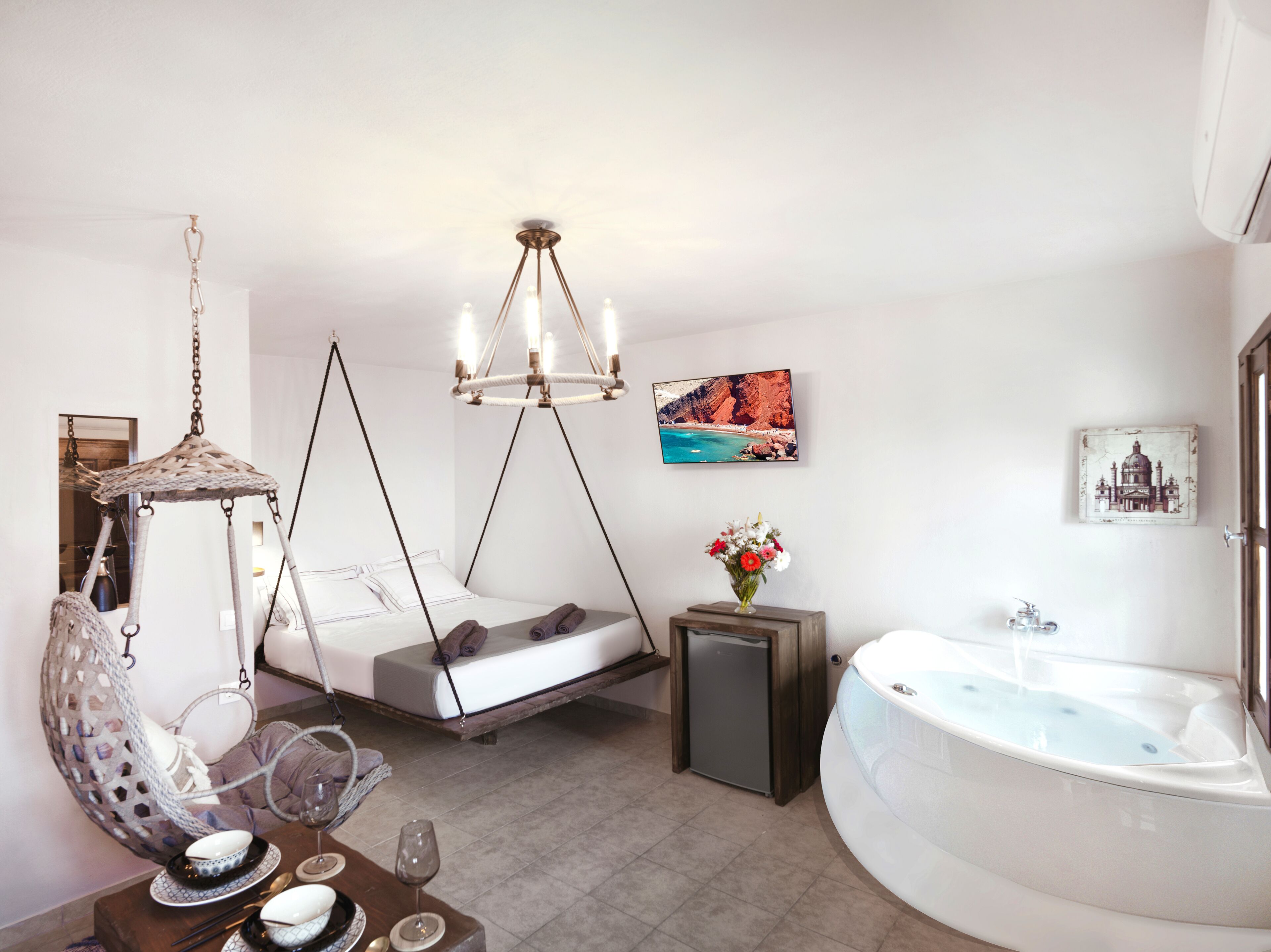A modern bedroom with a hanging chair, a bed with a unique design, a large window, and a bathtub.