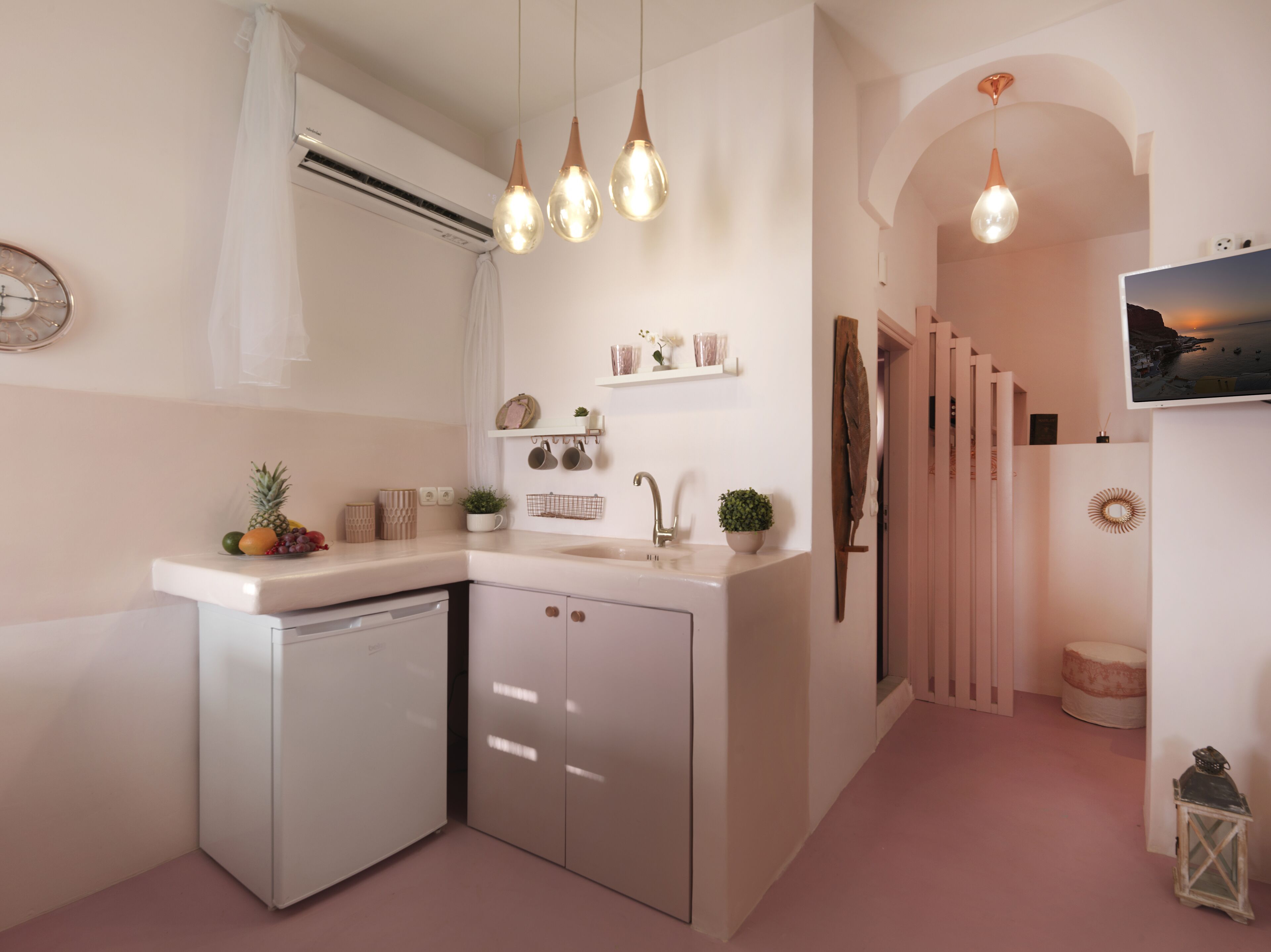 A modern kitchen with a dishwasher, a sink, and a fruit bowl. There is a small plant on the counter and a shelf with decorative items.