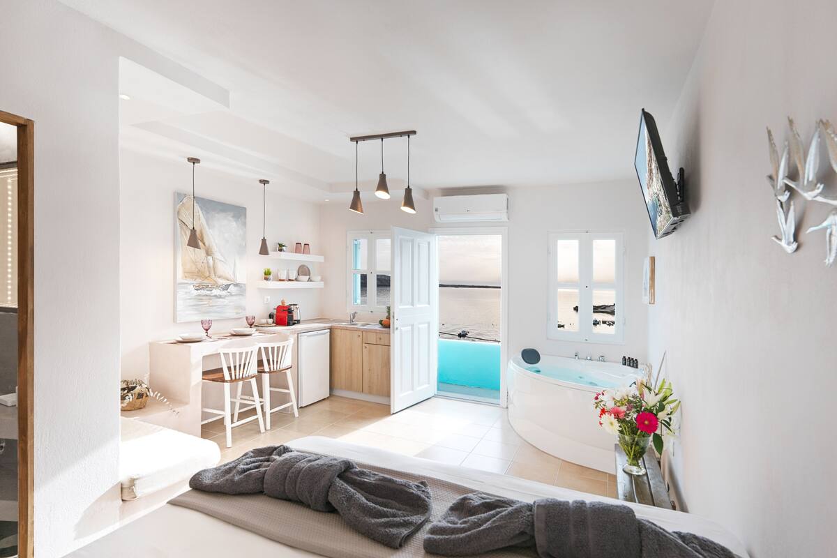 A modern kitchen with a view of the sea, a dining area with white chairs, and a large window.