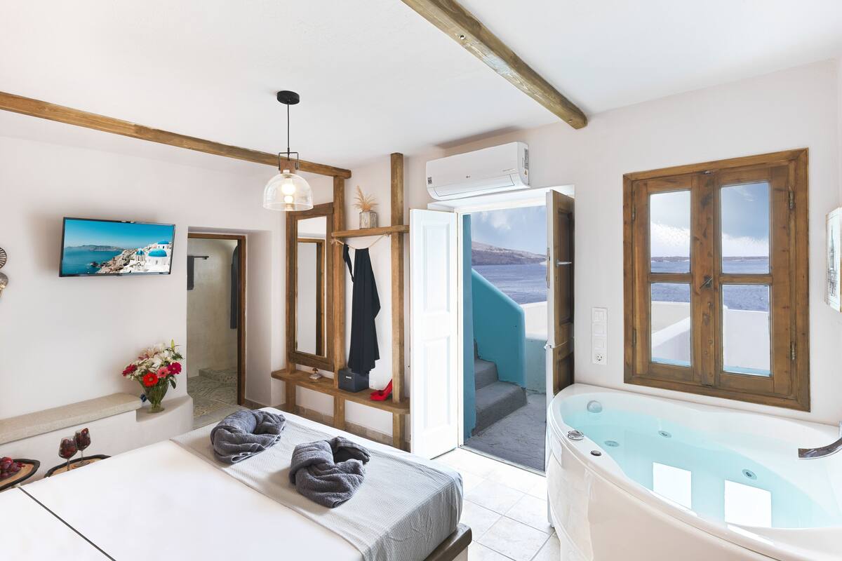 A room with a bed, a bathtub, a TV, and a view of the sea.