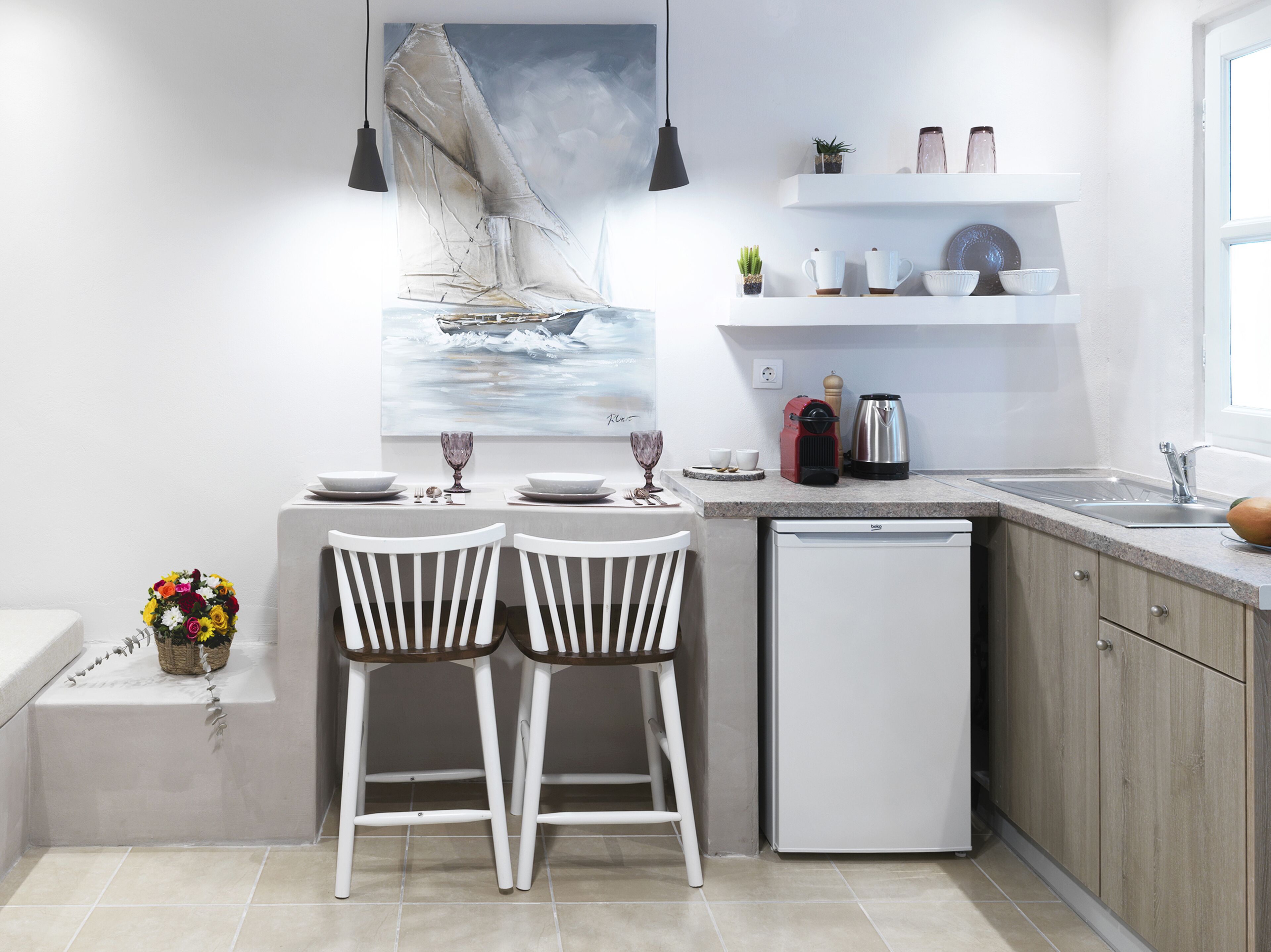 A modern kitchen with white cabinetry, a built-in dishwasher, and a dining area with two white chairs and a table set for two.
