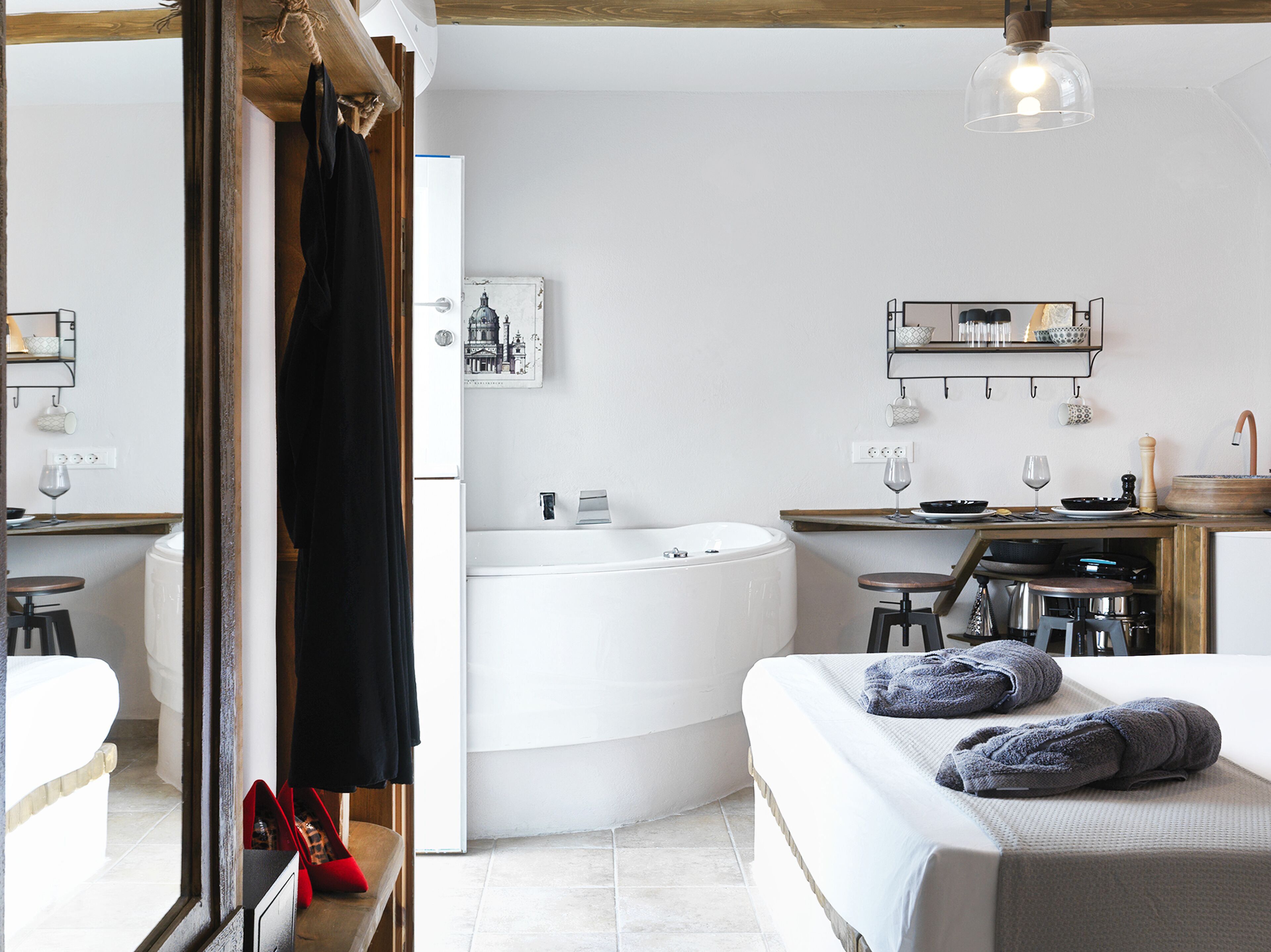 A modern bedroom with a large bed, a sitting area with a table and chairs, a bathtub, and a bathroom with a sink and mirror.