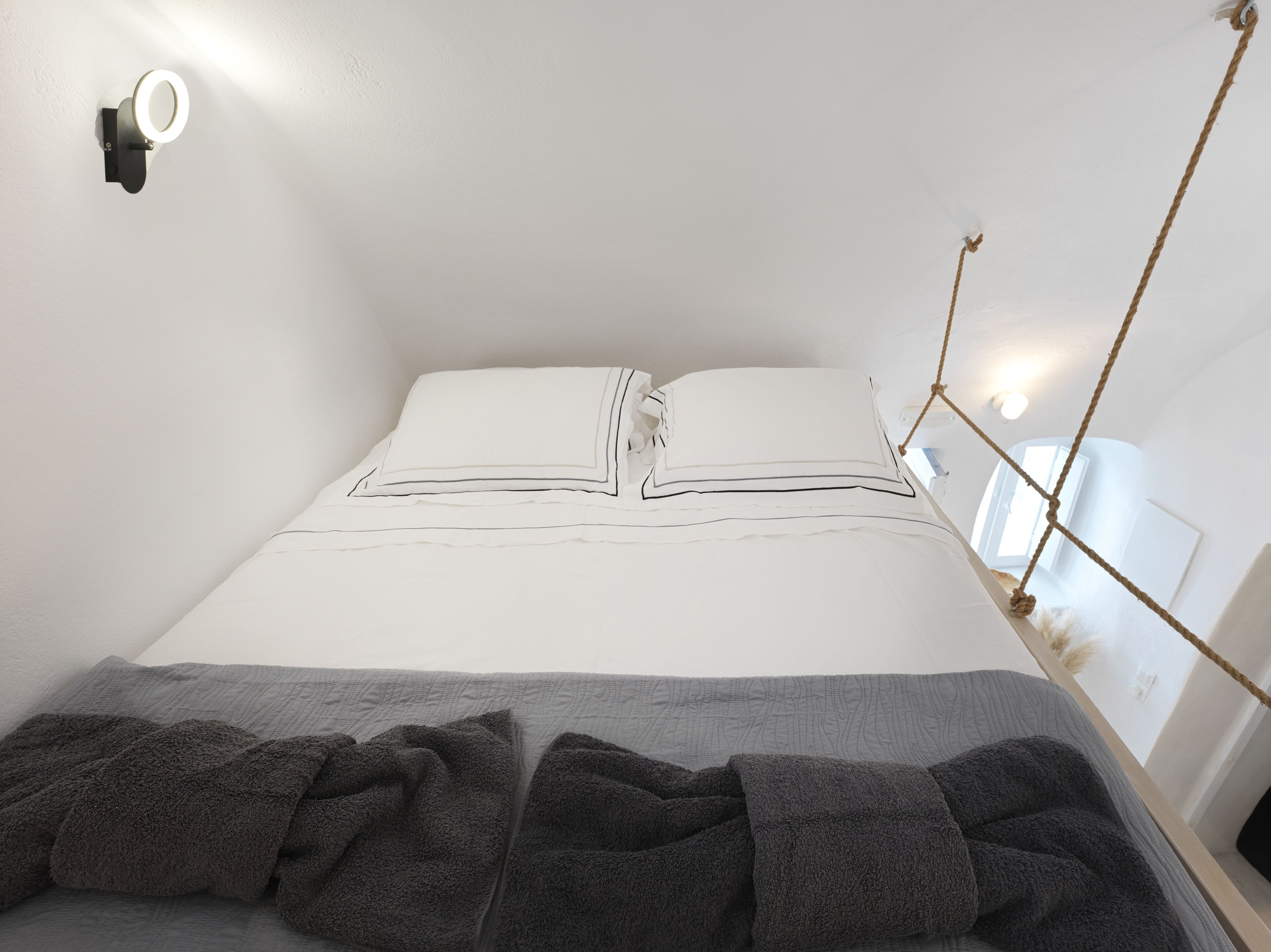 A neatly made bed with white bedding and a gray blanket, a wall-mounted light fixture, and a rope swing.