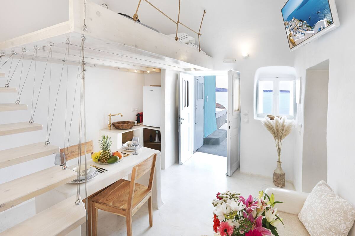 A modern kitchen with a dining area, a view of the sea, and a living room with a sofa and flowers.