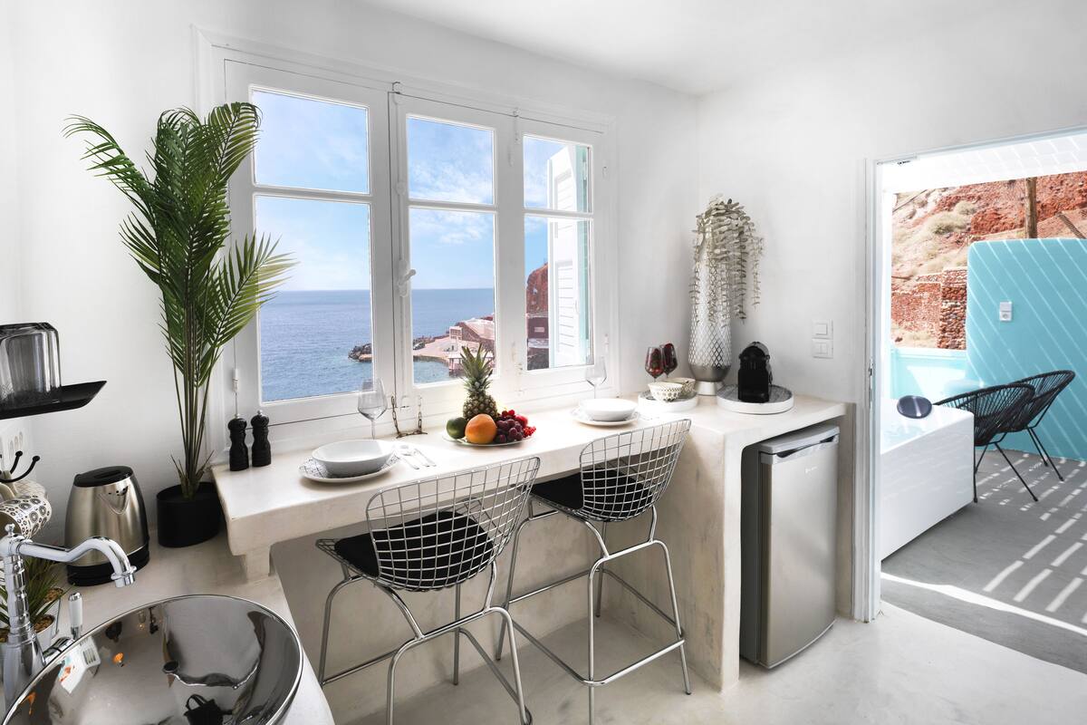 A modern kitchen with a large window overlooking the sea, a compact island, and a compact dishwasher.