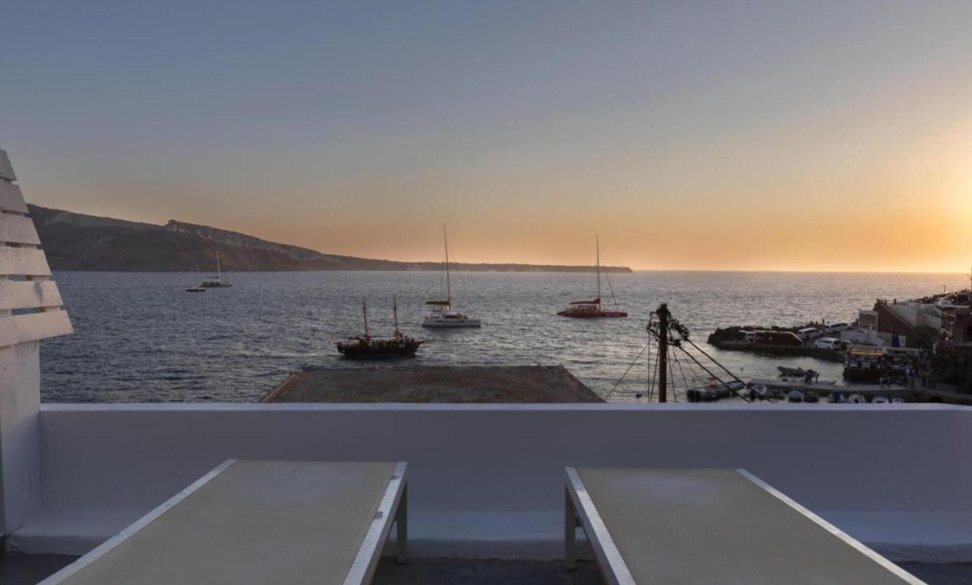 A seaside view from a balcony with a clear sky, boats on the water, and a distant shoreline.