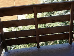 A wooden balcony railing with a view of trees and a building in the background.