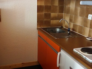 A kitchen with a stainless steel sink, a white stove, and orange cabinets.