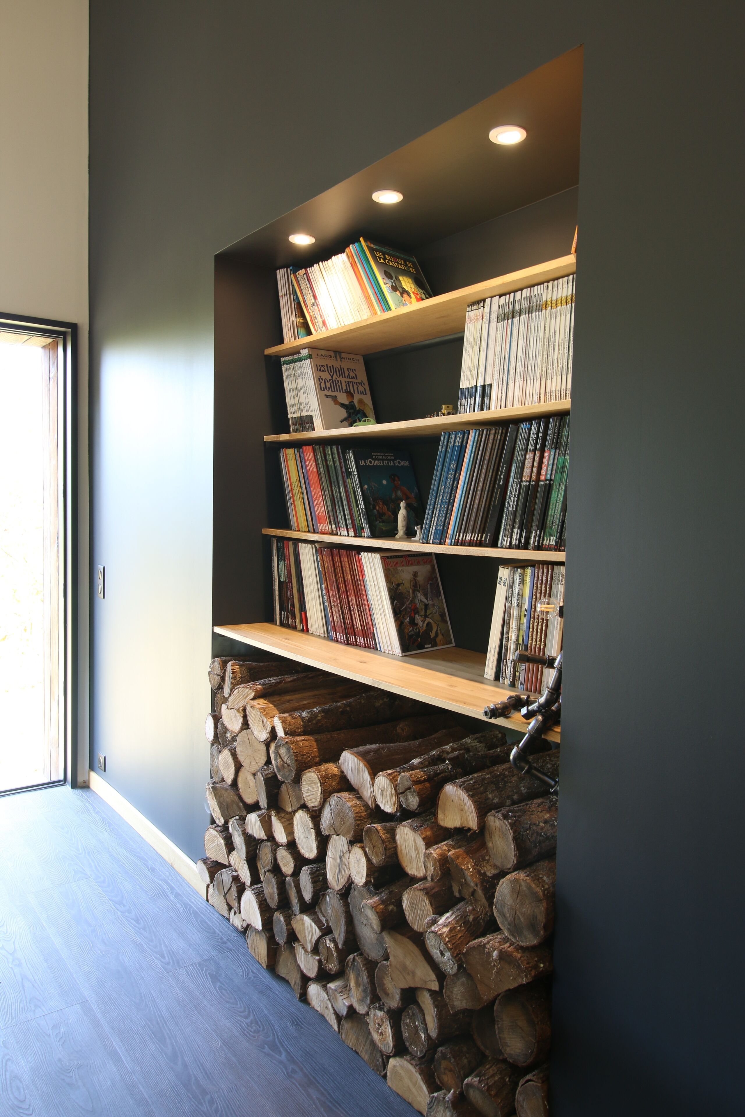 A bookshelf with various books and a stack of firewood against a wall.