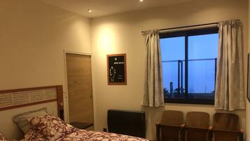 Une chambre à coucher avec un lit, un bureau, une chaise, une fenêtre avec des rideaux et une affiche accrochée au mur.