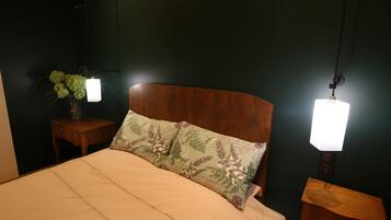 A bedroom with a wooden headboard, a bed with a beige bedspread, two bedside tables with lamps, and a wall-mounted plant.