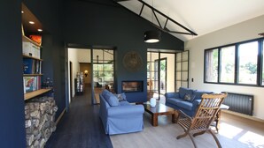 Una sala de estar moderna con un sofá azul, una mesa de centro de madera y un sillón mecedora. Hay una chimenea y una estantería llena de libros.