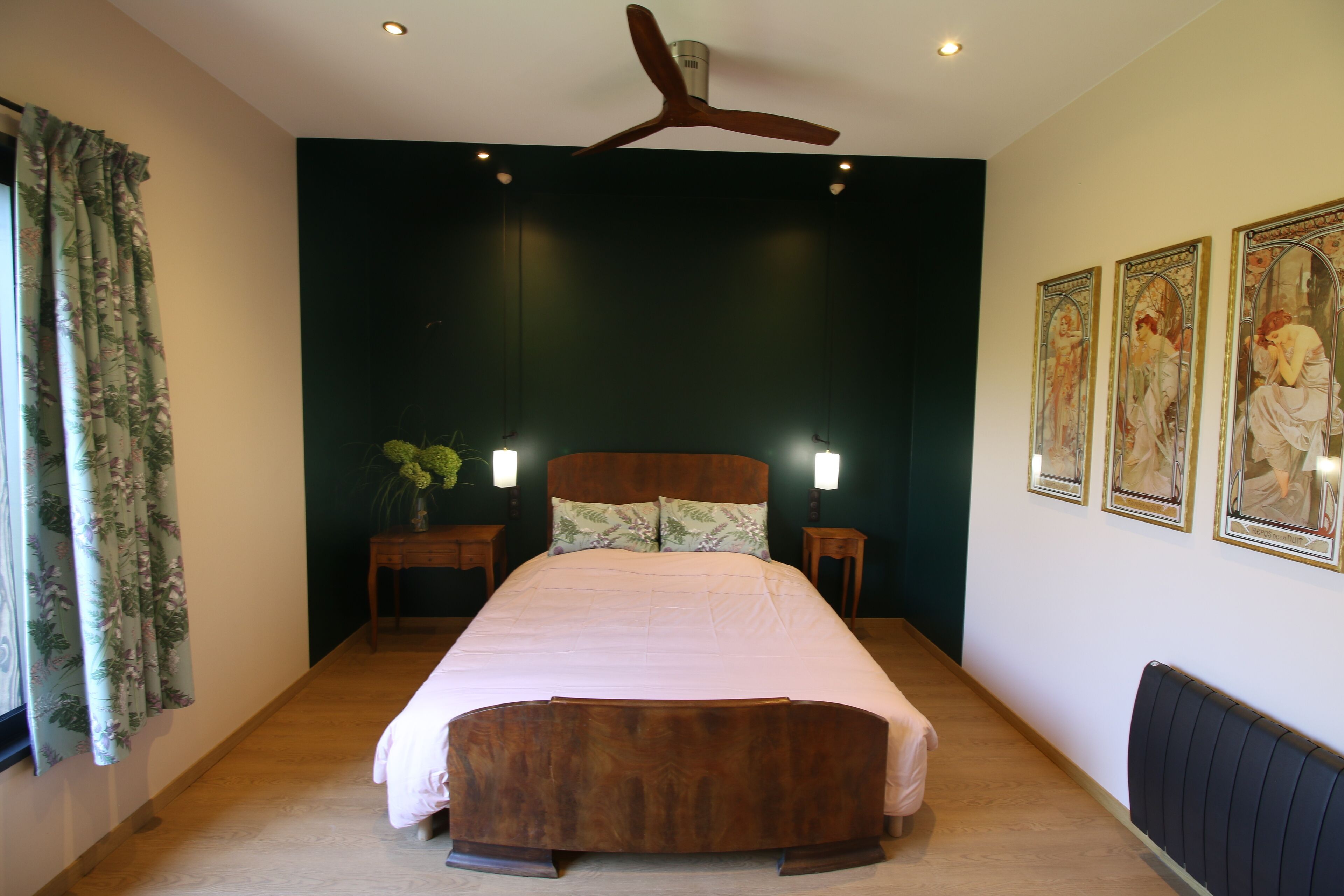 A bedroom with a large bed, two bedside tables, a ceiling fan, and three framed artworks on the wall.