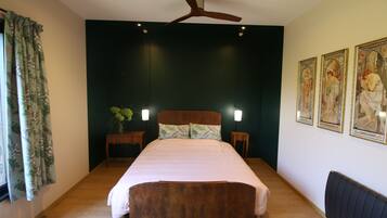 A bedroom with a large bed, two bedside tables, a ceiling fan, and three framed artworks on the wall.