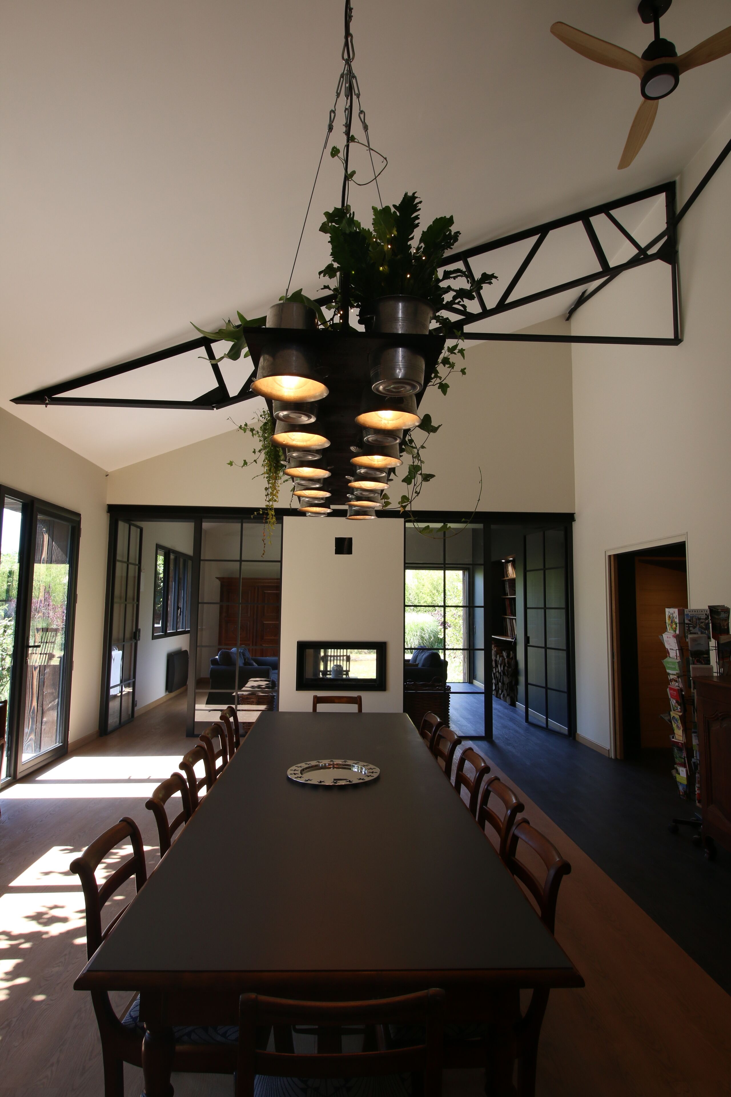 Un espace repas moderne avec une longue table, des chaises, des plantes suspendues et un ventilateur de plafond.