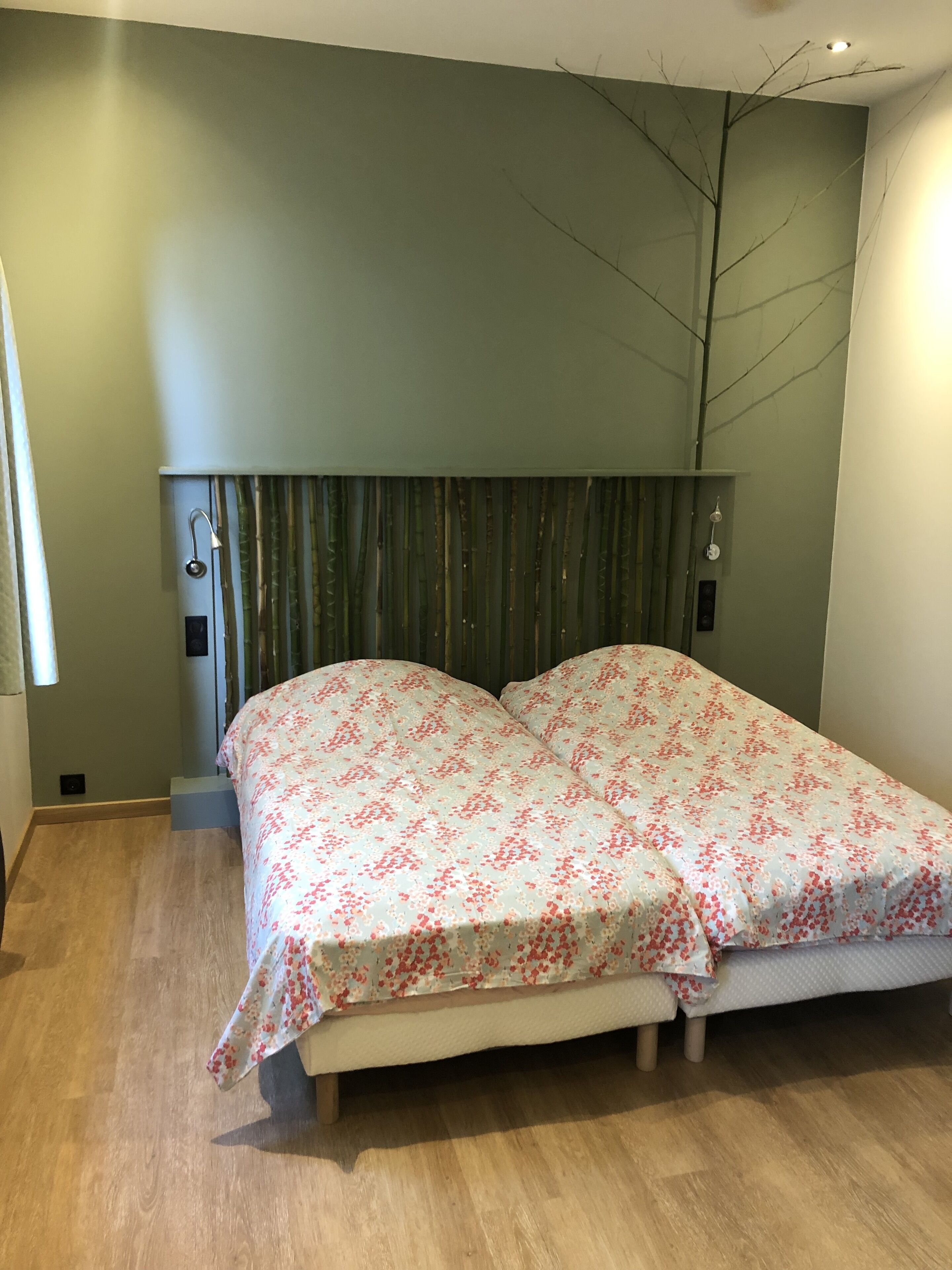 Un dormitorio con cama, cabecera, ventana y lámpara fijada a la pared.