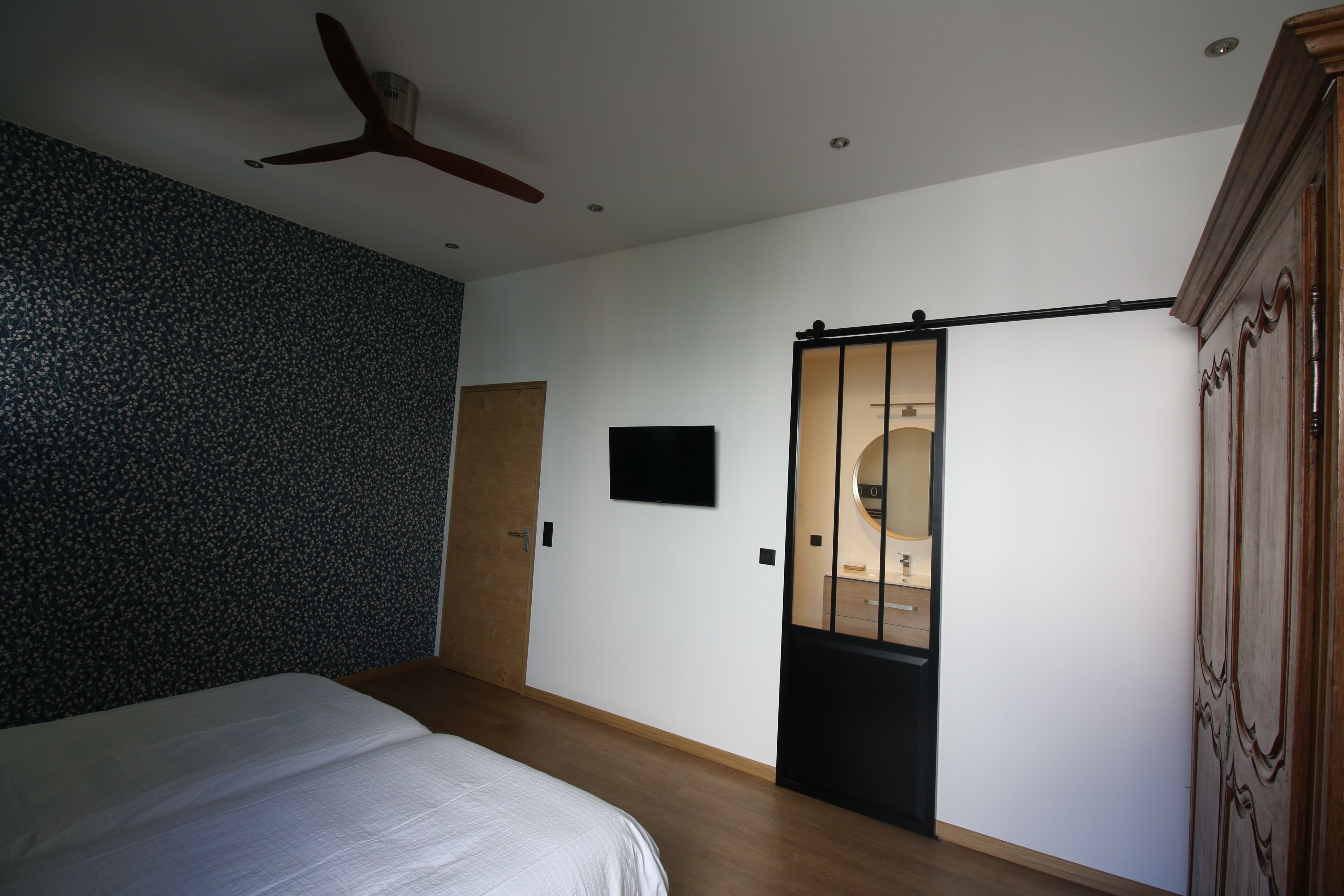 A bedroom with a bed, a ceiling fan, a TV, a sliding door, and a wooden wardrobe.