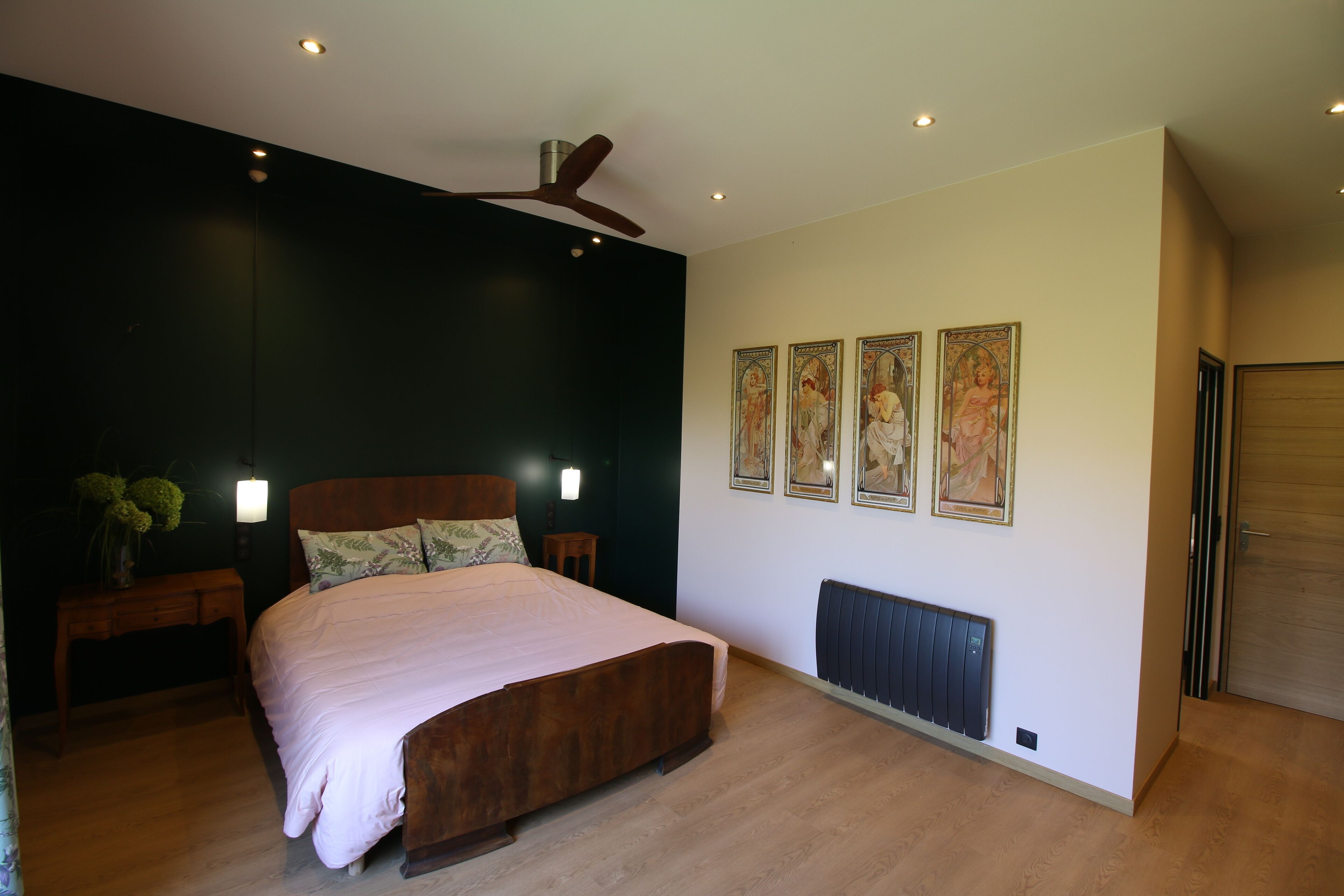 Une chambre à coucher comprenant un lit, une table de chevet, un radiateur fixé au mur et un ventilateur de plafond.