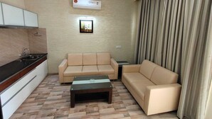 Ein modernes Wohnzimmer mit einem beigefarbenen Sofa, einem kleinen Couchtisch und einer Küchenzeile mit Schränken und Spüle.