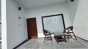 Ein kleiner, abgeschlossener Balkon mit einer Holztür, zwei Stühlen, einem Tisch und einem gerahmten Bild an der Wand.