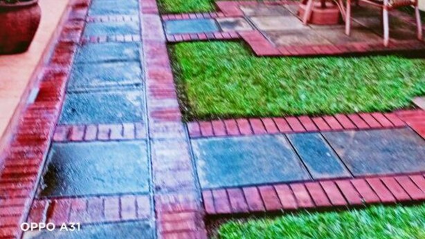 Un patio con un camino pavimentado, zona de estar exterior con mesas y sillas, y plantas en macetas.