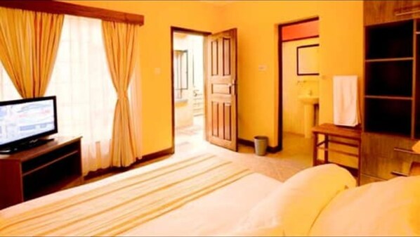 Habitación de hotel con cama, televisión, escritorio y baño visible a través de una puerta abierta.
