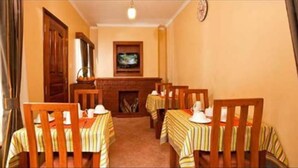 Un comedor con sillas y mesas de madera, una chimenea y un televisor en la pared.