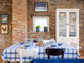 A dining area with a checkered tablecloth, white chairs, and a white cabinet with glass doors.