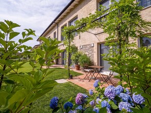 A well-maintained garden with hydrangea bushes, a patio with outdoor furniture, and a building with stone walls and large windows.