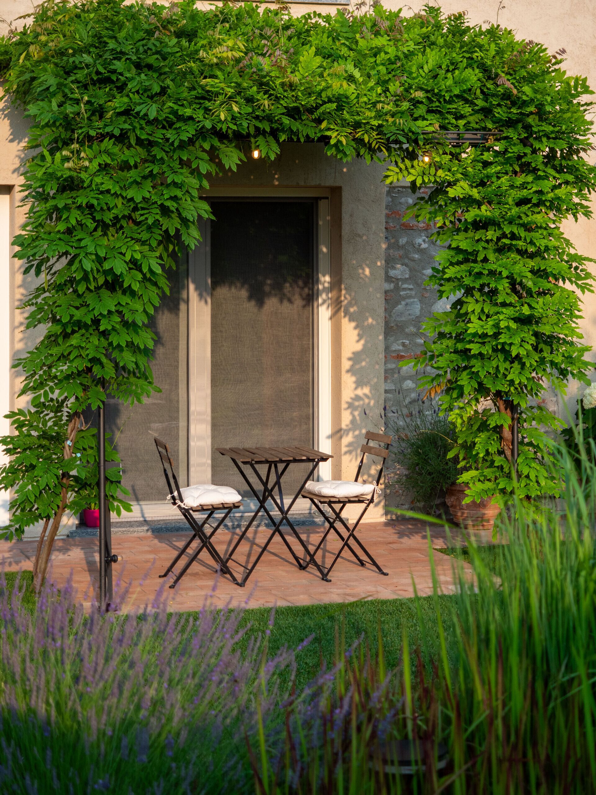 Un espace extérieur aménagé avec une table et des chaises, entouré de verdure et d’un mur en pierre.