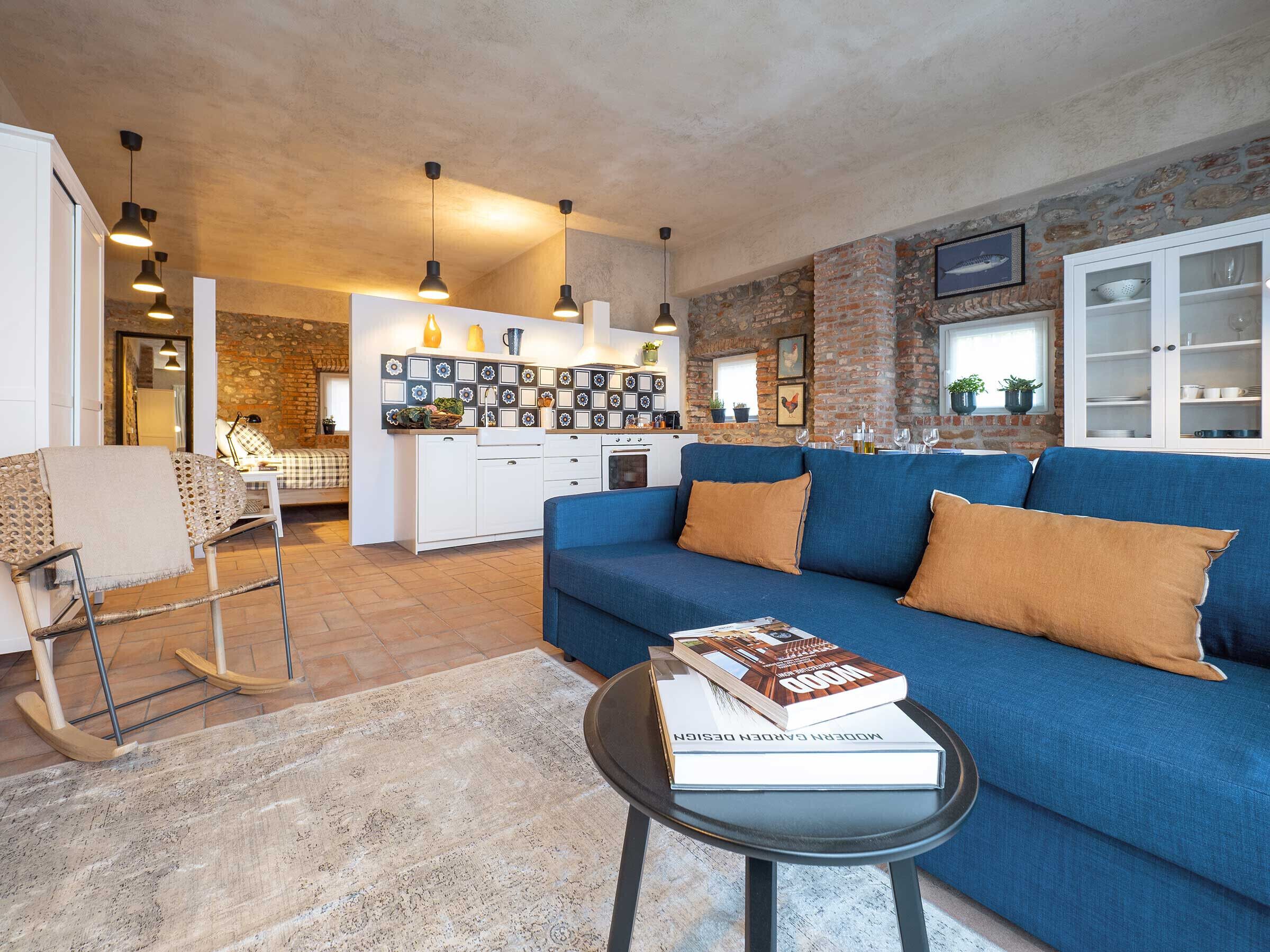 A modern living room with a blue sofa, a coffee table with a book, and a kitchen in the background.