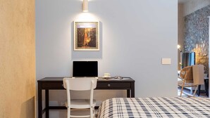Een moderne slaapkamer met een bed, een bureau met een laptop, een stoel en een lijstje aan de muur.