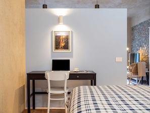A modern bedroom with a bed, a desk with a laptop, a chair, and a framed picture on the wall.