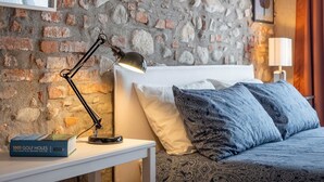 A room with a brick wall, a bed with patterned bedding, a desk with a lamp, and a book titled '1001 Golf Holes'. - Quiet Studio Apartment with Garden in Farmhouse (Cressa)