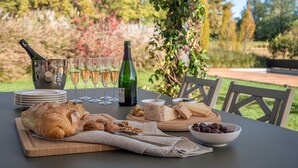 An outdoor dining setup with a table set for a meal, including bread, cheese, and a bottle of wine.
