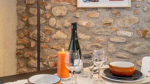 Una tavola imbandita con piatti, bicchieri, posate, una candela e una bottiglia di vino, con una parete in pietra sullo sfondo.