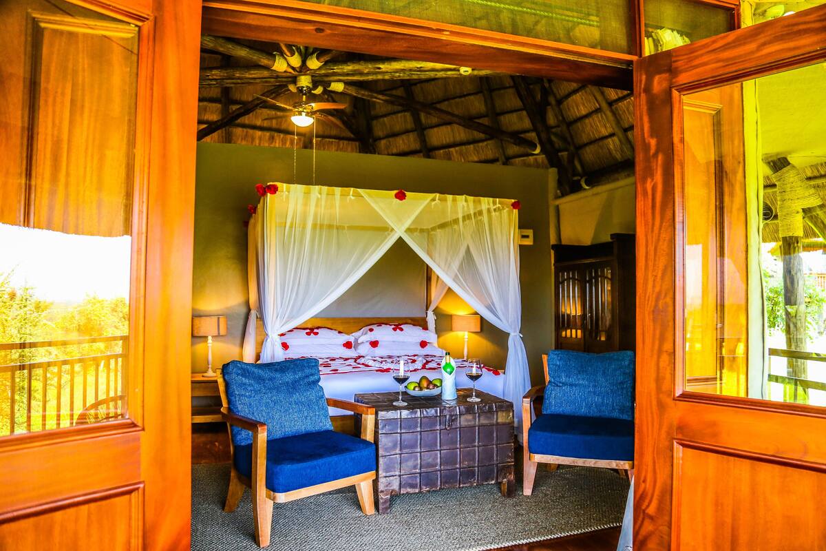 A room with a bed, two chairs, a small table, and a ceiling fan.