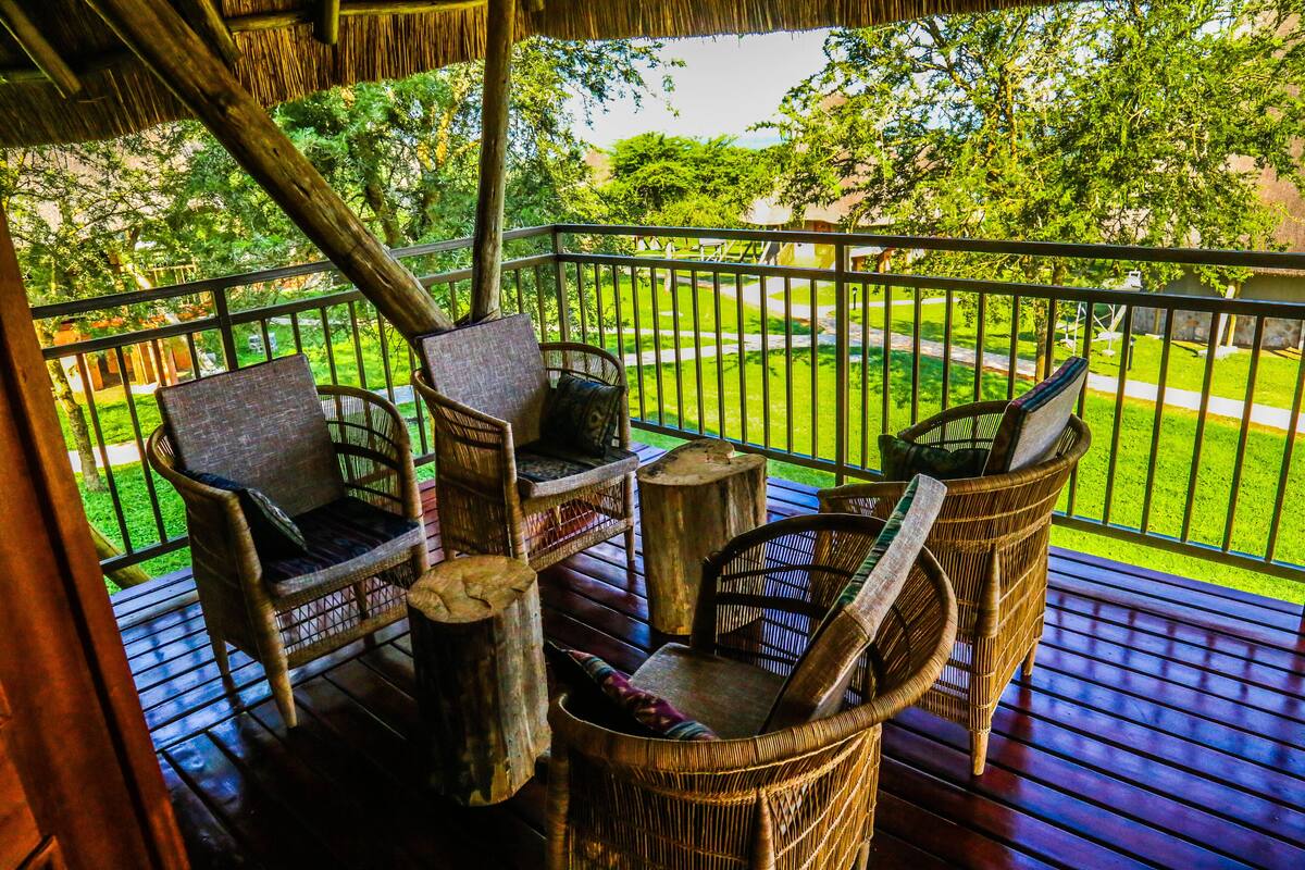 A wooden deck with wicker furniture, a thatched roof, and a view of a well-maintained lawn and trees.