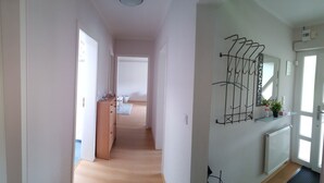 A hallway with a wooden floor, a radiator, a coat rack, and a door leading to a room with a bed and a window. - Pure relaxation with Nina (Bad Lauterberg im Harz)