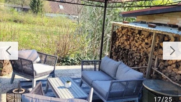 An outdoor seating area with wicker furniture and a table, a stack of firewood, and a covered structure. - Pure relaxation with Nina (Bad Lauterberg im Harz)