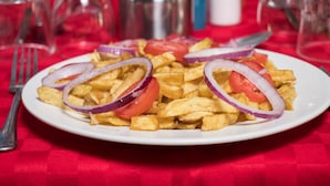 A plate of French fries with tomato and onion garnishes on a white plate, set on a red tablecloth. - Express Inn (Nyeri)